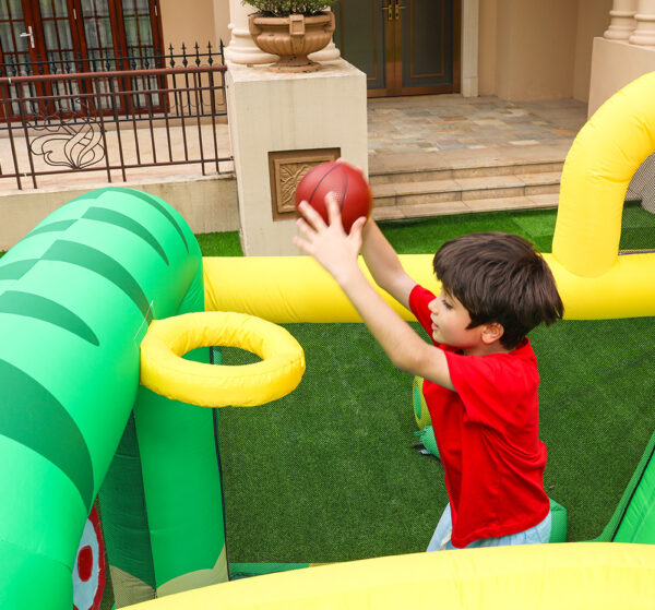 Boy playing basketball hoop inside dinosaur bounce house rental - fun party activity for kids