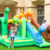 Kids playing on dinosaur themed bounce house with slide in backyard - bounce house rental Beaverton Oregon