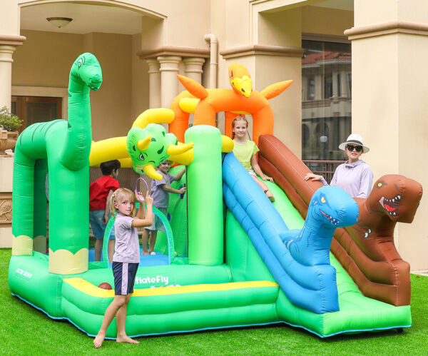 Kids playing on dinosaur themed bounce house with slide in backyard - bounce house rental Beaverton Oregon