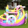 Kids playing on colorful unicorn rainbow bounce house with slide in backyard - bounce house rental Beaverton Oregon