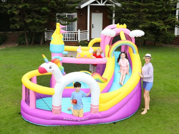 Kids playing on colorful unicorn rainbow bounce house with slide in backyard - bounce house rental Beaverton Oregon