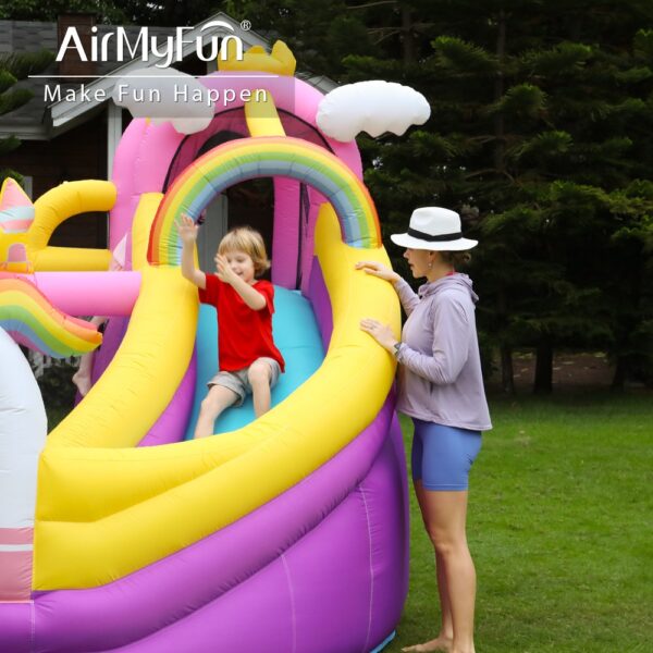 Child sliding down rainbow slide on dreamy unicorn bounce house while parent watches - bounce house rental Beaverton